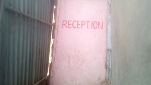 Un corridoio stretto con un cartello che indica 'RECEPTION' al muro, che conduce a una stanza con una finestra.