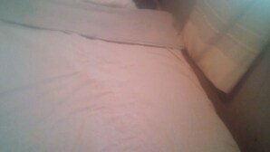 Un letto con lenzuola bianche in una stanza poco illuminata.