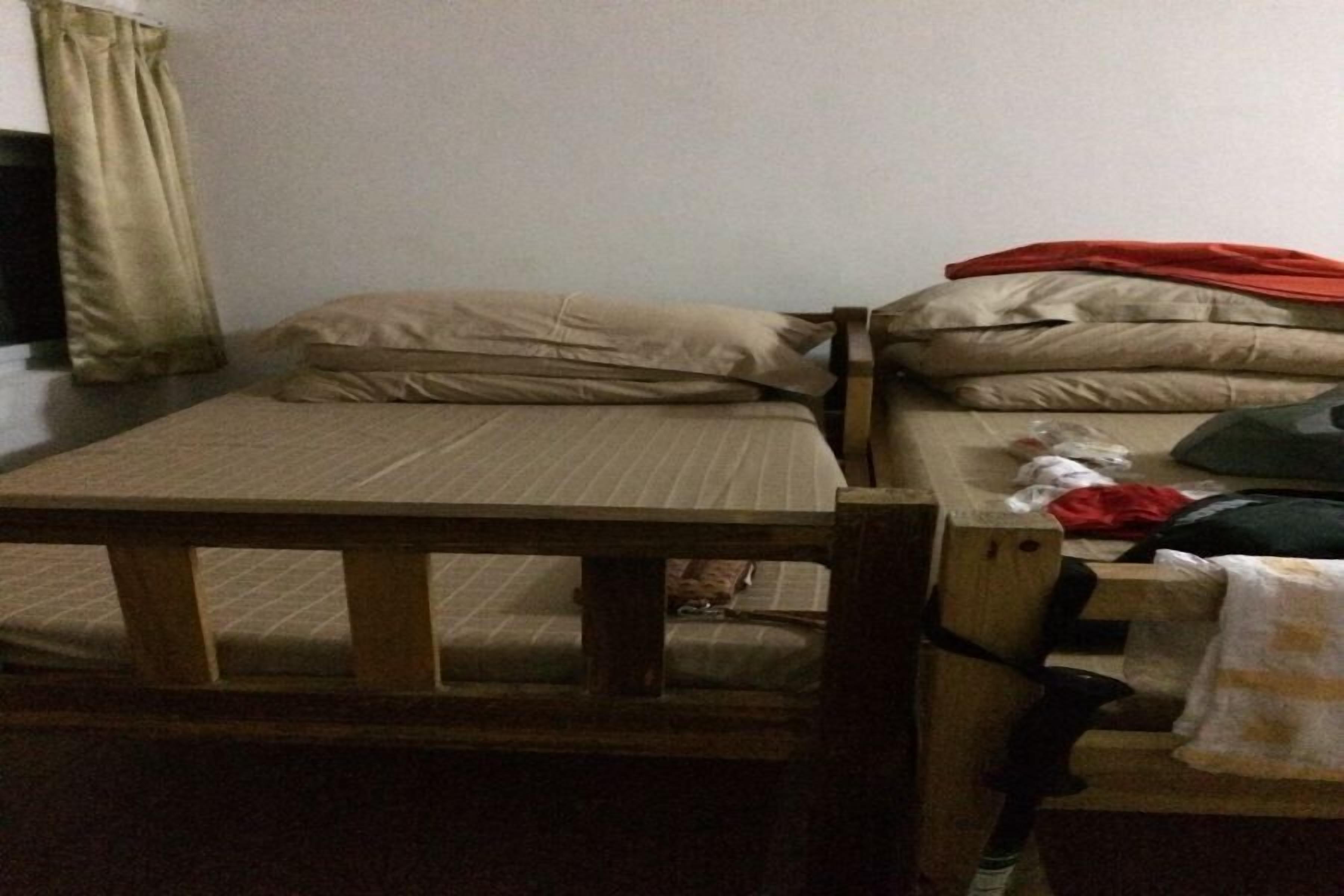 A single bed with a wooden headboard, a small table, and a window with curtains.