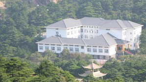 A multi-story building with a symmetrical roofline, surrounded by dense greenery and rocky cliffs. - Huangshan Baiyun Hotel (Huangshan)