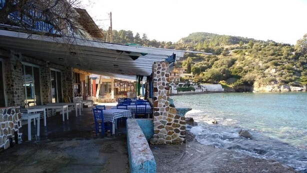 A seaside restaurant with outdoor seating, stone walls, and a view of the sea and hills. - Palm tree house by the beach (Λουτράκι)