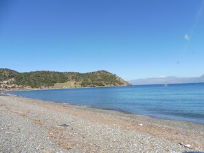 Une plage de galets offrant une vue dégagée sur la mer et sur une chaîne de montagnes lointaine.