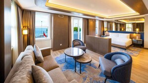 A modern hotel room with a sofa, armchairs, a small table, a bed, and a view of the sea. - Radisson Hotel Istanbul Sultanahmet (Istanbul)