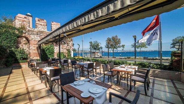 An outdoor dining area with tables set for two, overlooking a body of water and historic stone structures. - Radisson Hotel Istanbul Sultanahmet (Istanbul)