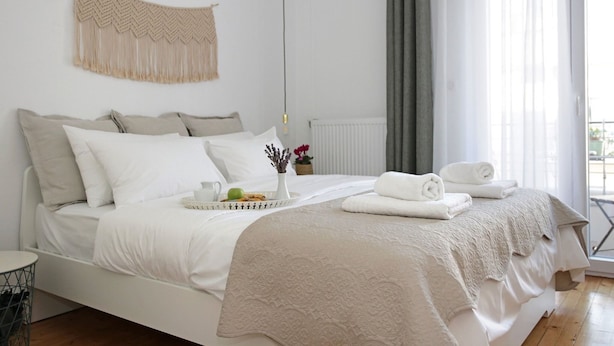 A neatly made bed with white linens, a tray with fruits and a vase of flowers, and a view of the outdoors through a window. - Lena's Central Relaxed Eco Apartment (Thessaloniki)