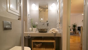 A modern bathroom with a toilet, sink, and shower. There is a mirror above the sink and a shelf below it. - Lena's Central Relaxed Eco Apartment (Thessaloniki)