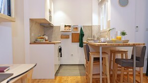 A compact kitchen with a dining area, wooden flooring, and a clock on the wall. - Lena's Central Relaxed Eco Apartment (Thessaloniki)