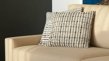 A beige sofa with a textured pillow, a round black coffee table with two glasses, and a black and white striped rug.