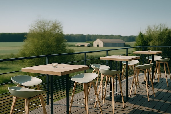 Um terraço com mesas e cadeiras, com vista para uma paisagem verde e um edifício ao longe.