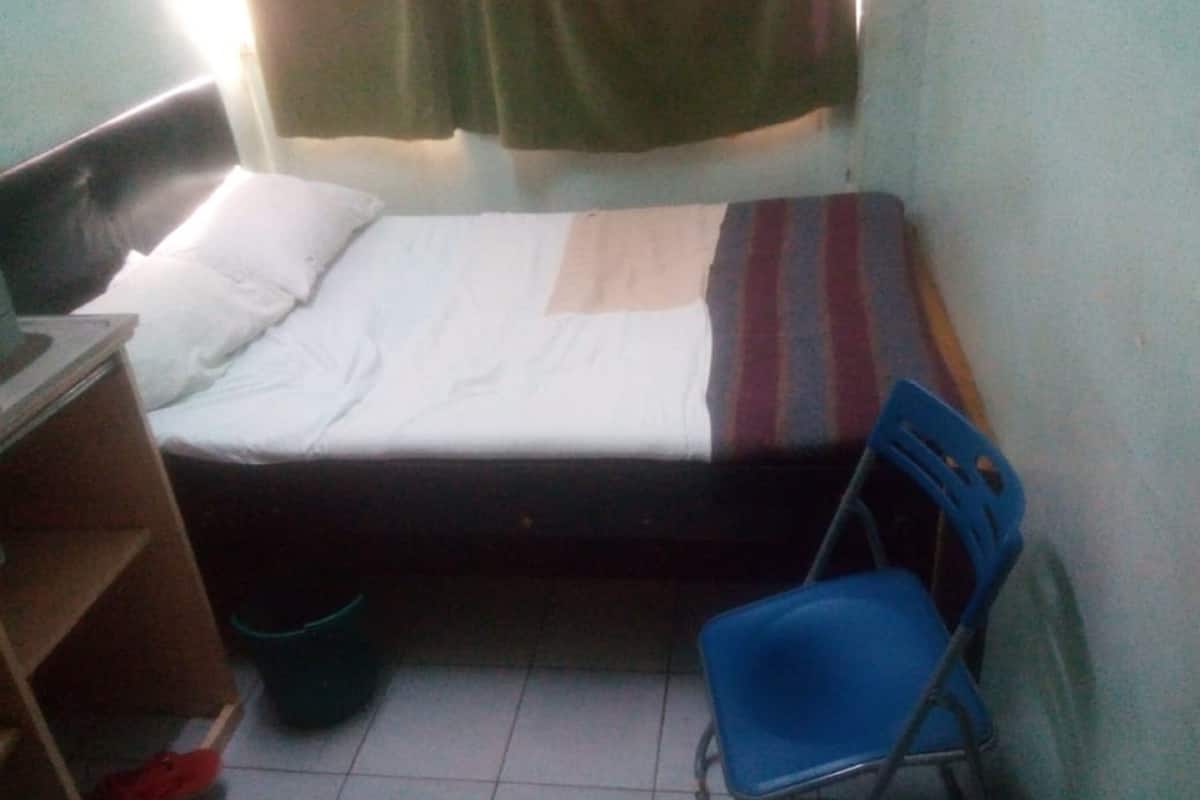 Una habitación pequeña con cama individual, cabecera de madera, una silla azul y una mesita.