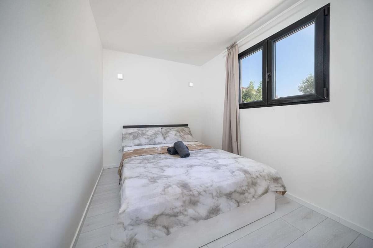 Un dormitorio con cama, ventana y vista a árboles.