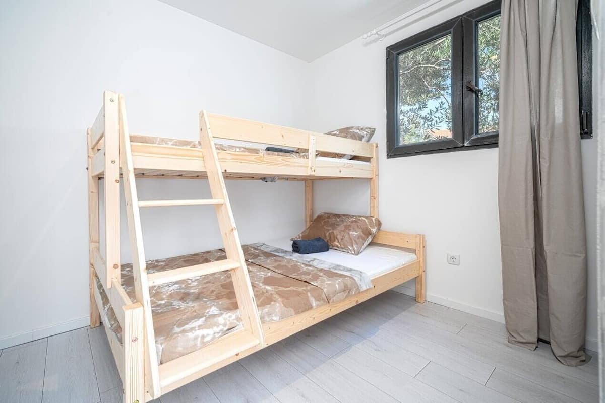 Una cama litera en una habitación con paredes blancas y una ventana con cortinas.