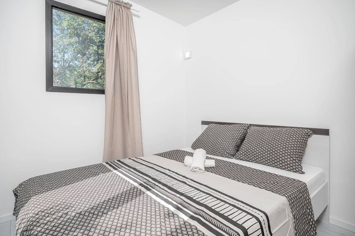 Un dormitorio con cama, ventana y vista a árboles, además de una cortina.