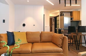 Una sala de estar moderna con un sofá de cuero, un comedor con mesa y sillas, y una cocina con armarios de madera y un refrigerador.