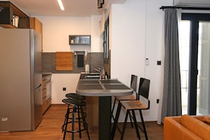 Una cocina compacta con una isla central, taburetes de bar, un refrigerador y un comedor con sillas.