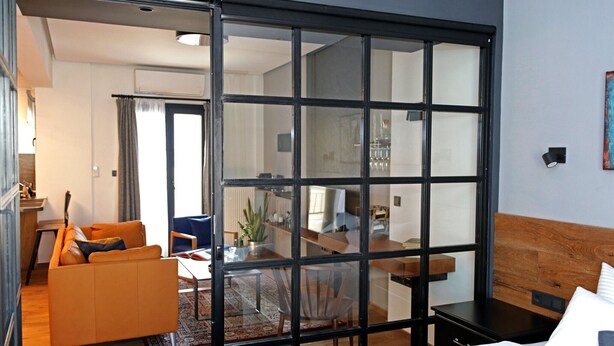 Una habitación de hotel moderna con una puerta de cristal corredera que da a un comedor, un sofá, una cama y una mesita.
