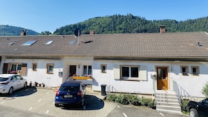 Un bâtiment à deux étages, doté d’un toit recouvert de tuiles, d’une entrée avec une porte en bois et d’un espace de stationnement pouvant accueillir deux voitures.