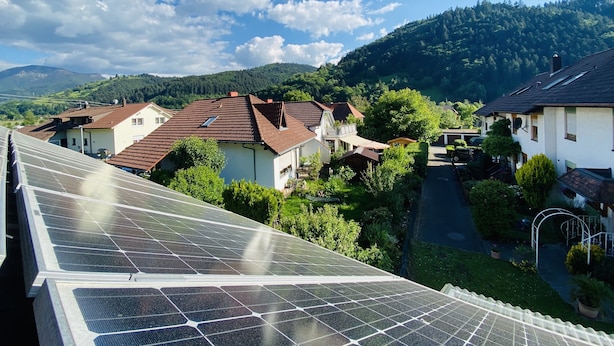 Un quartier résidentiel avec des maisons, un ensemble de panneaux solaires et une chaîne de montagnes en arrière-plan.