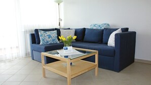 En stue med en blå sofa, et glasbord og en vase med gule blomster.