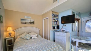 Une chambre à coucher comprenant un lit, des tables de chevet, un téléviseur, une bibliothèque et une petite table avec des chaises.