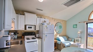 Une cuisine compacte avec des meubles blancs, un four à micro-ondes, un réfrigérateur et un évier. On y trouve également un coin repas avec une table et des chaises, ainsi qu’une fenêtre donnant sur l’extérieur.