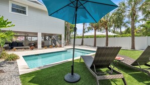 Un jardin avec une piscine, un patio couvert et des chaises longues.