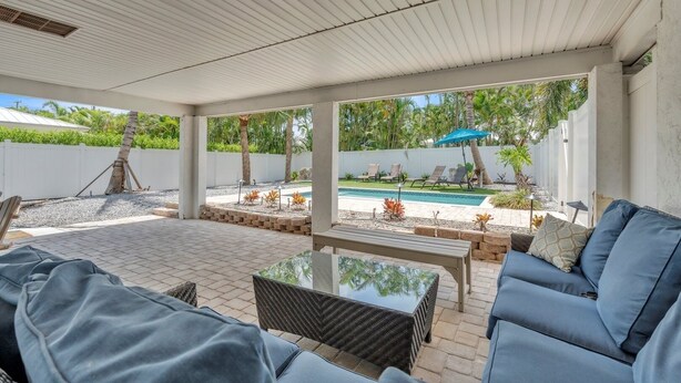Un patio couvert avec une piscine, des sièges d’extérieur et une vue sur le jardin arrière.