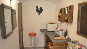 Una cucina compatta con uno sgabello da bar, un tostapane, bicchieri da vino e un termosifone.