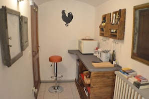 A compact kitchen with a bar stool, a toaster, wine glasses, and a radiator.