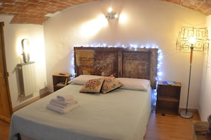 A bedroom with a bed, bedside tables, a nightstand, a lamp, and a brick wall.