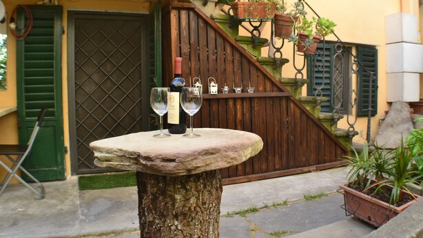 Un tavolo in pietra con una bottiglia e bicchieri di vino, una scala in legno e piante in vaso.
