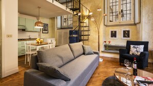 A modern living room with a grey sofa, a dining area with a table and chairs, a staircase leading to an upper level, and a large window with a view. - Cool Loft Deluxe by Dante House, Top Location (Florence)