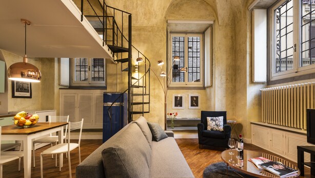 A spacious living area with a staircase, a sofa, a dining table with chairs, and a coffee table with a magazine and glasses. - Cool Loft Deluxe by Dante House, Top Location (Florence)