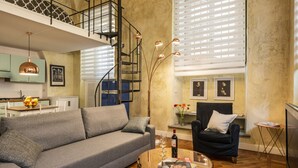 A modern living room with a grey sofa, a coffee table with a magazine, a wine bottle, and a staircase leading to an upper level. - Cool Loft Deluxe by Dante House, Top Location (Florence)