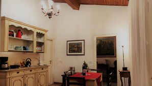 Un coin repas avec une table en bois, des chaises et un lustre. On y trouve un buffet rempli de vaisselle et un tableau accroché au mur.