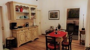 Un coin repas avec une table en bois, des chaises, un meuble contenant de l’ustensile de cuisine et un tableau accroché au mur.