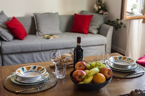 A dining table with a bowl of fruit, plates, glasses, and a bottle of wine.
