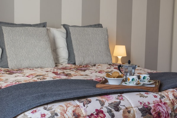 A neatly made bed with floral bedding, a bedside table with a lamp, and a tray with breakfast items.