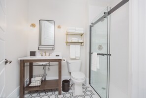 A modern bathroom with a glass shower enclosure, a white toilet, and a wooden vanity with a sink and mirror.