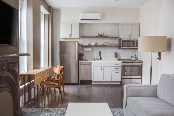 A modern kitchen with white cabinets, a microwave, and a built-in oven. There is a dining area with a wooden table and chairs.
