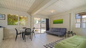 A spacious living area with a dining table, chairs, a sofa, and a green bed. - The Black Shack - Cooks Beach Holiday Home (Cooks Beach)