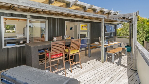 A covered outdoor dining area with wooden furniture and a view of the surrounding landscape. - The Black Shack - Cooks Beach Holiday Home (Cooks Beach)