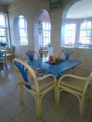 A dining area with a blue table and wicker chairs, a tiled floor, and arched windows.