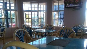 Comedor con mesas y sillas redondas, ventanas amplias y un televisor en la pared.