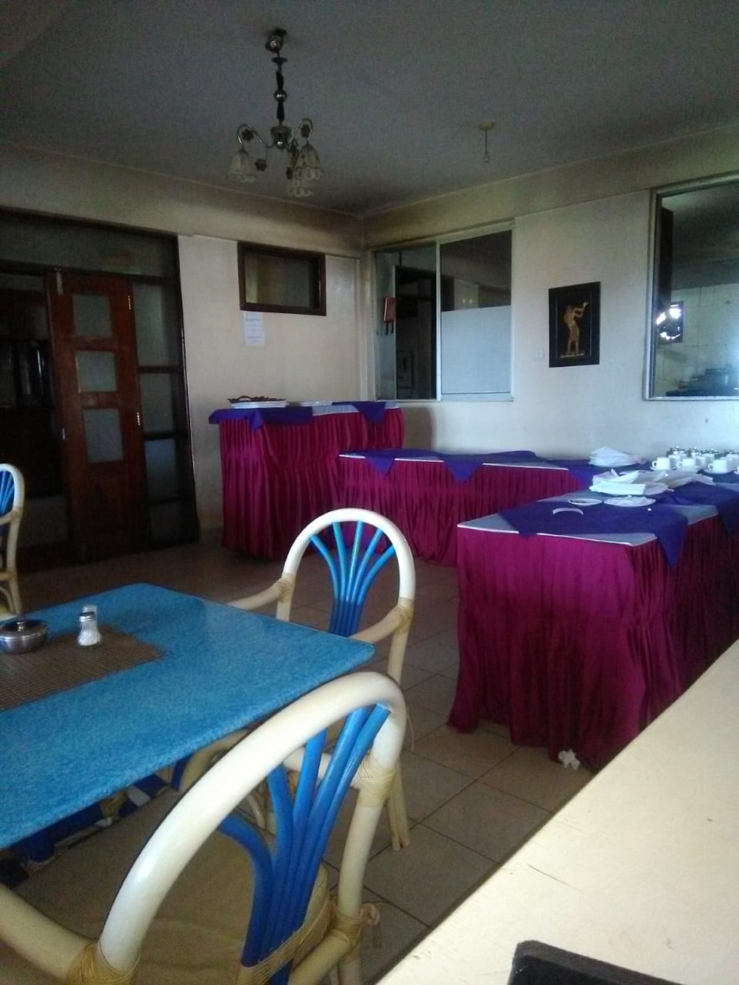 Un salón de conferencias con mesas cubiertas con manteles rojos y azules, sillas blancas y una araña.