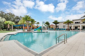 Una piscina con scivolo, palme e sdraio.