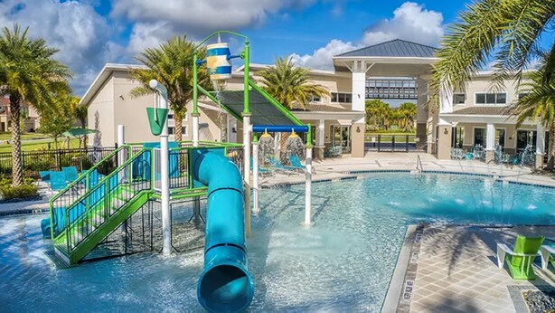 Uma área de piscina com escorregador, palmeiras e um edifício com varanda coberta.