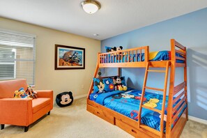 Une chambre d’enfant avec un lit superposé, une petite chaise orange et une couverture de lit aux motifs de Mickey Mouse.