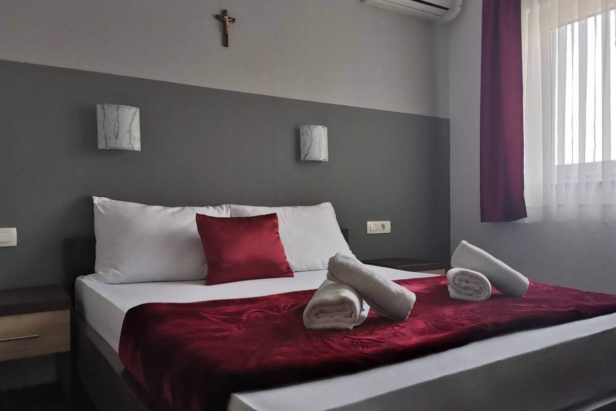 Une chambre d’hôtel avec un lit, un plaid rouge et deux oreillers blancs.