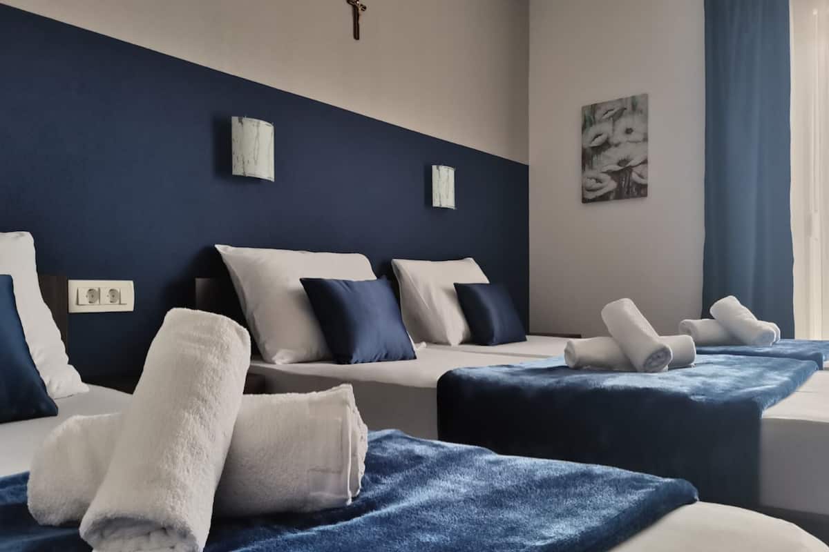 Une chambre d’hôtel avec deux lits, chacun recouvert d’une couverture bleue et agrémenté de serviettes blanches. On y trouve des appliques murales et un tableau accroché au mur.